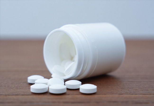 Белая пластиковая баночка с таблетками лежит на боку на деревянной поверхности
